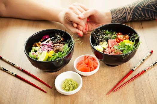 Loving couple man and woman eating salad poke chopsticks. Place the tuna salad in a bowl. People in the restaurant eat salad with chopsticks. Asian seafood salad concept