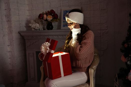 Happy young woman with a present, opening a Christmas present box. Portrait of happy smiling girl opening gift box isolated on red background