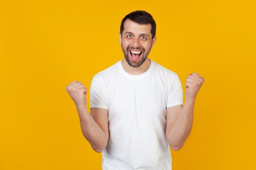 I won. Victory of success. Happy man celebrates being a winner. Dynamic image of a caucasian guy with a beard on a yellow studio background. Victory, delight concept. The concept of human emotions.