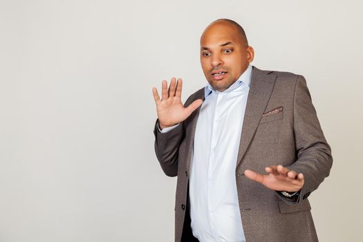 Portrait of shocked young African American businessman guy, scared and frightened by fear expression, stopped hand gesture, shouting in shock. Panic concept. Standing on a gray background