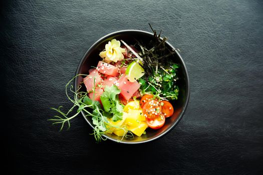 Poke salad with tuna in a bowl. Ingredients fresh tuna, cherry tomatoes, marinated seaweed, rice, takuan, Ponzu sauce, Teriyaki sauce, nori, sesame seeds, lime, cilantro. Asian seafood salad concept