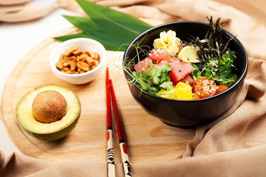 Poke salad with tuna in a bowl. Ingredients fresh tuna, cherry tomatoes, marinated seaweed, rice, takuan, Ponzu sauce, Teriyaki sauce, nori, sesame seeds, lime, cilantro. Asian seafood salad concept