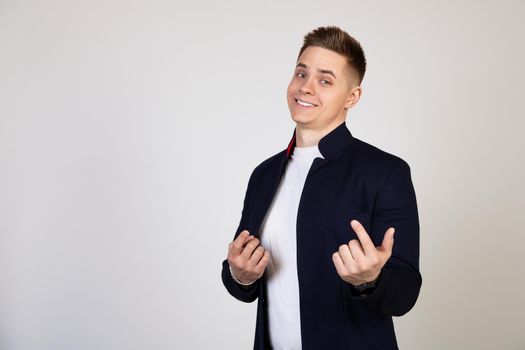 A young man, a handsome guy beckons to him with a finger. Come closer twitching a finger, beckons to come up to him, standing on a white background looks at the camera.