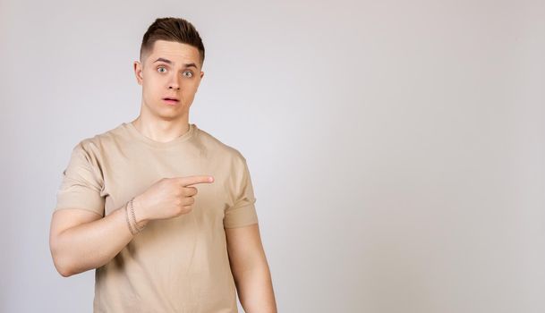 The man the guy points to the side with a displeased face. Young doubter man, holds his hand and points to the side with forefingers at blank space