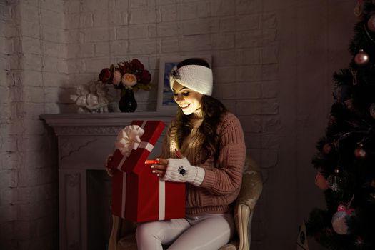 Happy young woman with a present, opening a Christmas present box. Portrait of happy smiling girl opening gift box isolated on red background