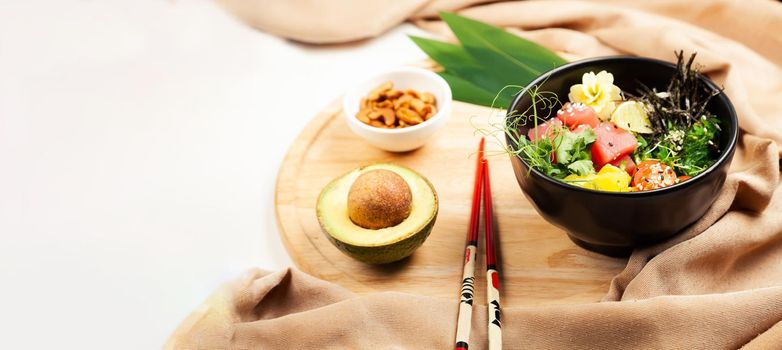 Poke salad with tuna in a bowl. Ingredients fresh tuna, cherry tomatoes, marinated seaweed, rice, takuan, Ponzu sauce, Teriyaki sauce, nori, sesame seeds, lime, cilantro. Asian seafood salad concept