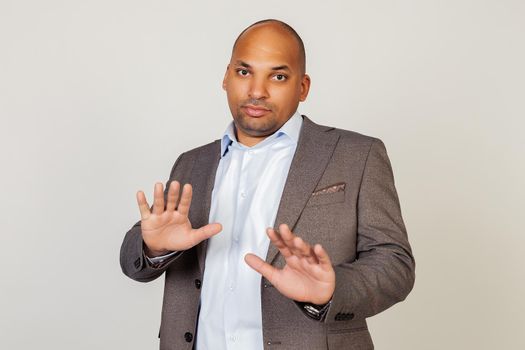 Portrait of shocked young African American businessman guy, scared and frightened by fear expression, stopped hand gesture, shouting in shock. Panic concept. Standing on a gray background