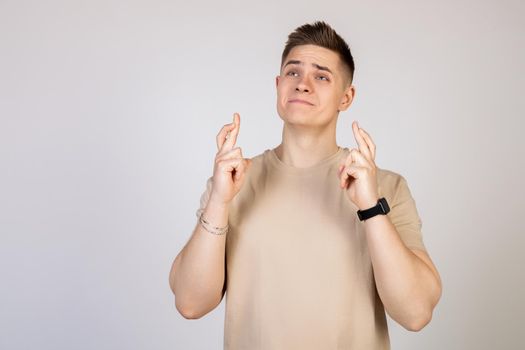 Photo of a young, nervous, excited man with his fingers crossed. Man holding fingers crossed with worried facial expression.