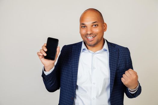 Young african american man showing smartphone screen, shouting with pride and celebrating victory and success, very excited, rejoice emotion.