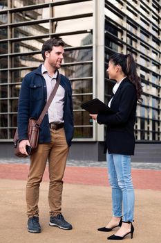 caucasian man and asiatic woman talking about business in front of an office building, concept of coworkers and lifestyle