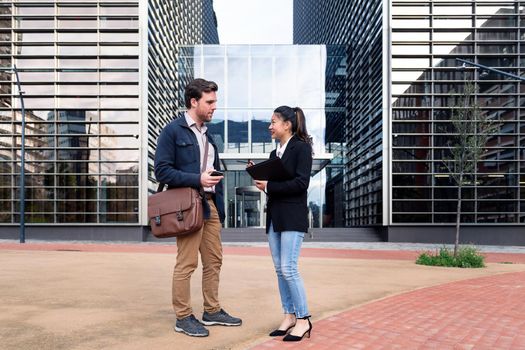 caucasian man and asiatic woman talking about business in front of the entrance to an office building, concept of coworkers and lifestyle, copy space for text