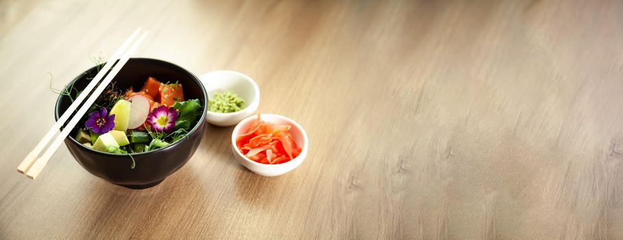 Poke salad with salmon in a bowl next to wasabi and ginger. Ingredients fresh salmon, avocado, cucumber, rice, Tamarind sauce mango sauce nori lime, sesame seeds, cilantro. Asian seafood salad concept