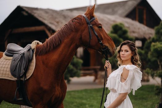 Beautiful girl in a white sundress next to a horse on an old ranch.