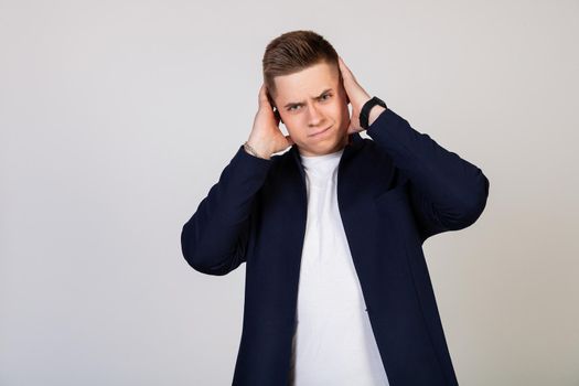A young man covering his ears with his hands, he does not want to listen to news, gossip, information. Bearing terrible pain. Young guy covered his ears with his hands so as not to hear rumors.