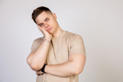 Young handsome guy holding his head with his hand, tired after a long and hard working day, standing on a white background looking at the camera.