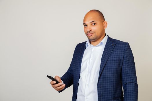A young African American man is using a smartphone with a confident expression on his face. African American looks at phone screen, reads news in message with mobile social network device