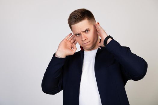 A young man covering his ears with his hands, he does not want to listen to news, gossip, information. Bearing terrible pain. Young guy covered his ears with his hands so as not to hear rumors.