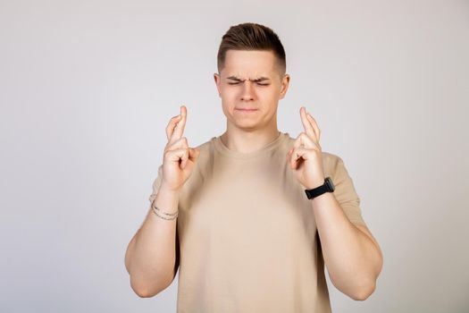 Photo of a young, nervous, excited man with his fingers crossed. Man holding fingers crossed with worried facial expression.