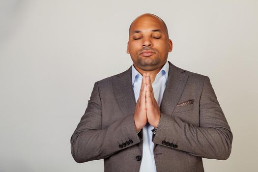 Man makes palms pressed together in praying gesture. Portrait of a concentrated black guy holding his hands together in front of his face, praying and hoping for the best. A man praying to god.