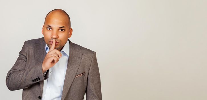 An African American man makes a gesture of silence, holds his finger to his lips, be quiet, don't tell anyone, makes a hand gesture, asking them to remain silent and not to tell about the secret