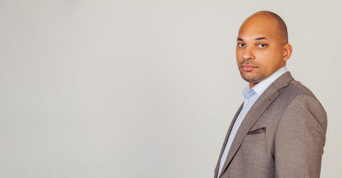 African American man looking into the camera with a serious expression. Business man businessman in classic suit looking at camera while standing on gray background