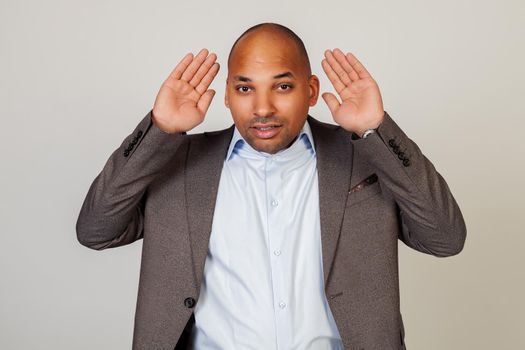 Man African American businessman, holding his hand behind his ear, showing that he does not hear, trying to listen to gossip, listen carefully to someone else's conversation.