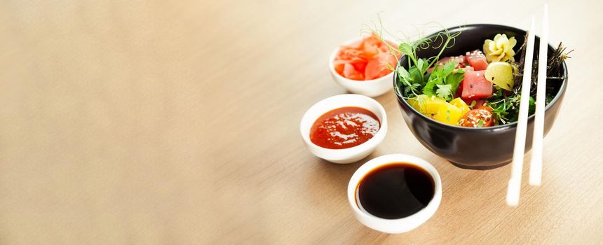 Poke salad with tuna in a bowl. Ingredients fresh tuna, cherry tomatoes, marinated seaweed, rice, takuan, Ponzu sauce, Teriyaki sauce, nori, sesame seeds, lime, cilantro. Asian seafood salad concept