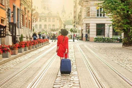 Beautiful young girl is walking with blue suitcase on the tram track road of the street of old European city.