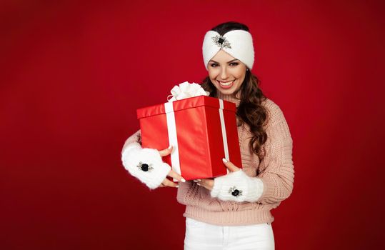 Happy woman holding a gift box. Portrait of happy smiling girl looking at delivered wrapped box isolated on red background