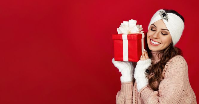 Happy woman holding a gift box. Portrait of happy smiling girl looking at delivered wrapped box isolated on red background