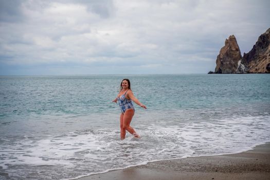 A plump woman in a bathing suit enters the water during the surf. Alone on the beach, Gray sky in the clouds, swimming in winter