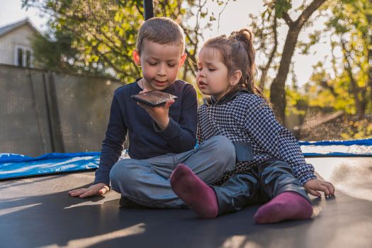 children look at the phone while sitting on a trampoline