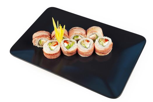 Sushi roll with bacon and fried sea bass on a black plate, ingredients fried sea bass, cream cheese, bacon, Iceberg salad, flying fish roe, Teriyaki sauce, rice, nori. For the restaurant menu