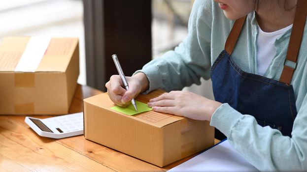 Start up business entrepreneur writing address on cardboard box. Online selling, E-commerce concept.