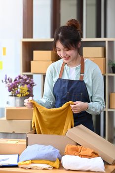 Happy small business owner packing product in cardboard box for delivery to customers. Online selling, E-commerce concept.