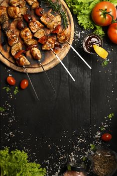 Delicious barbecue skewers with fresh vegetables on black rustic wooden table.