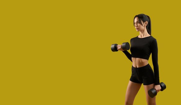 Side view of pretty slim girl standing, raising dumbbells. Brunette young woman making step, working out, stretching, looking forward. Isolated on yellow studio background.