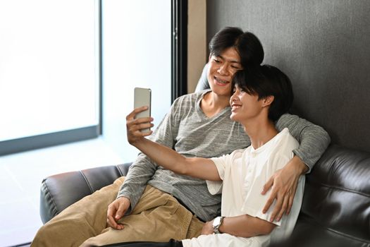Loving male lgbt couple making selfie while relaxing on sofa at home.