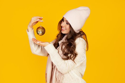 Happy young smiling woman holding a christmas tree ball promoting a best offer christmas tree. A girl in a sweater looks at a Christmas tree toy. New year and christmas holiday concept