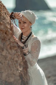 Middle aged woman looks good with blond hair, boho style in white long dress on the beach decorations on her neck and arms