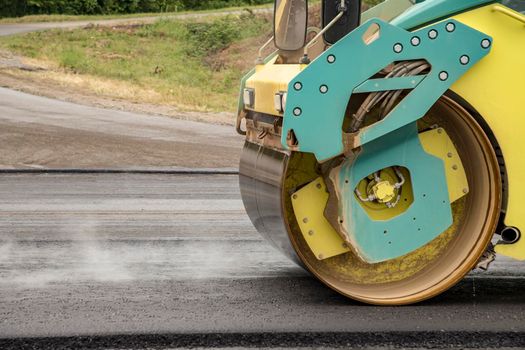 New asphalt road. the yellow road roller working on the new road with smoke. 