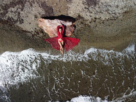 Young sensual blonde woman sitting on the rock near water at sea and enjoys the sea waves on background of two volcanic rocks, like in Iceland. Dreams holidays and weekend vacation in summer time