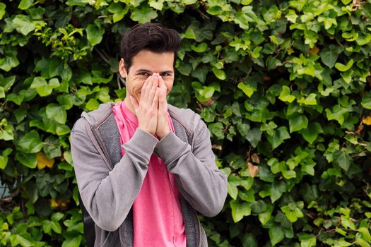 happy young man laughing covering his mouth with the hands on a green plants background, concept of fun expressions and emotions, copy space for text