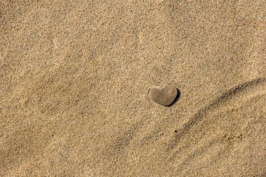 A small stone in the form of heart lies on the sand. 