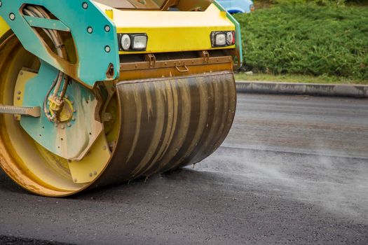 Close view of drum roller at the construction site, working on the new road with smoke