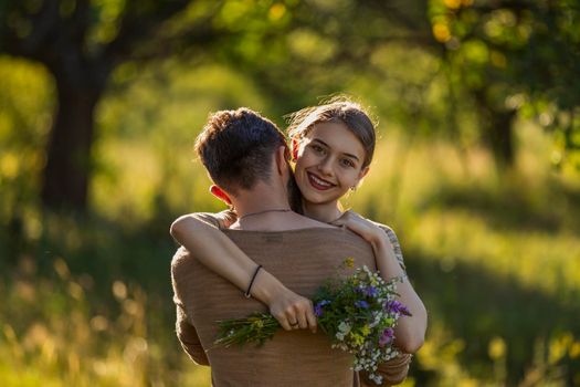 young couple hugging in nature, girl holding flowers