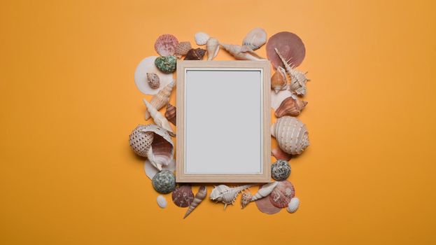 Empty picture frame with seashells on yellow background. Travel, summer and holiday concept.