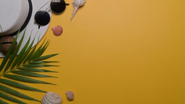 Traveler accessories, seashells and tropical palm leaves on yellow background with copy space. Travel, summer and holiday concept.