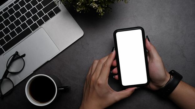 Woman hand holding smart phone with blank screen at modern workplace.