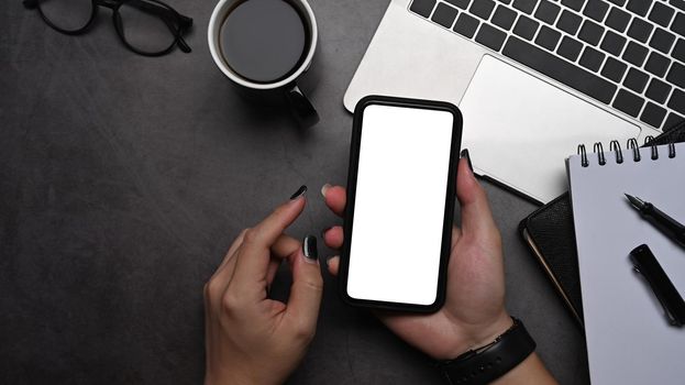 Above view woman hand holding mobile phone with empty screen at her stylish workplace.